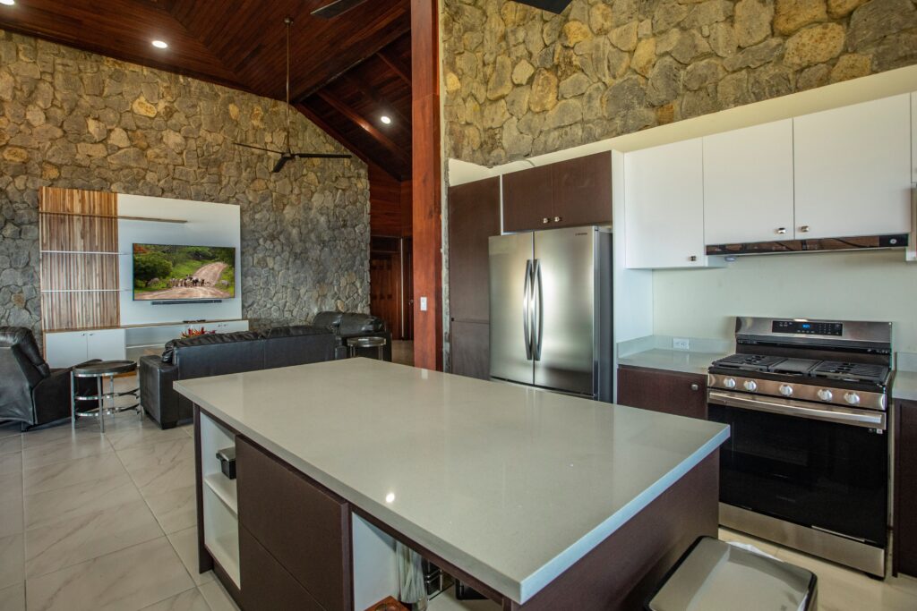 Modern kitchen with a large white island, stainless steel appliances and adjoining stone-walled living room