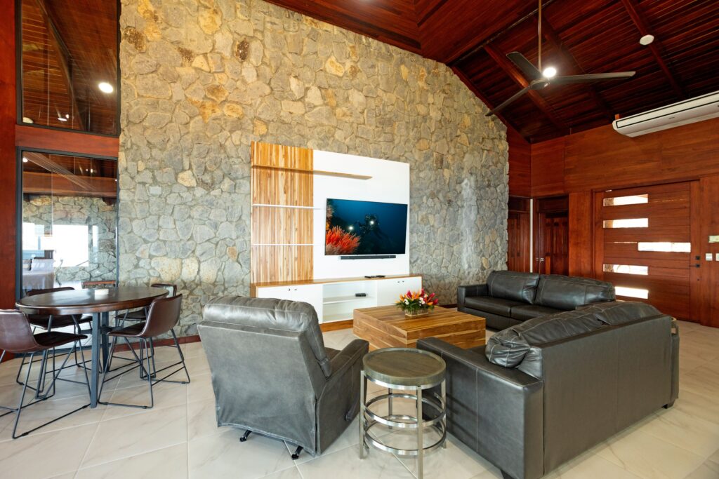 Stone-walled living room with black leather sofas, a wall-mounted TV and wooden front door