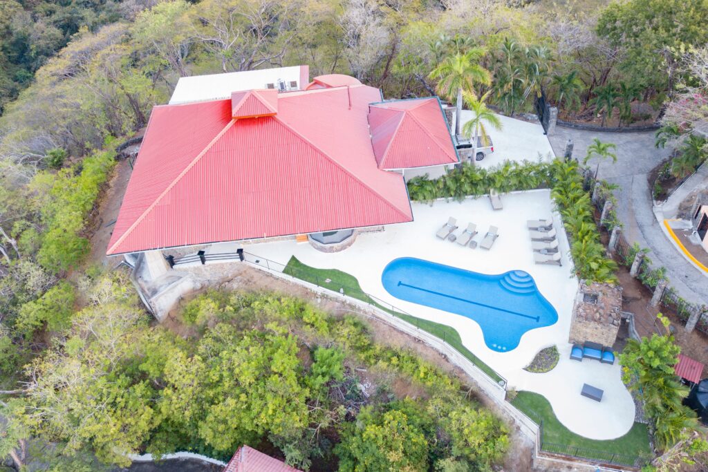 Aerial view of Villa Puerto Escondido, showing its red roof, curved swimming pool and surrounding tropical forest