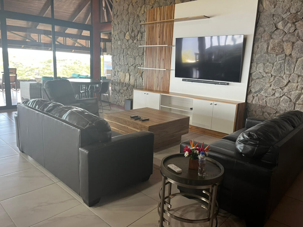 Living room with black leather sofas facing a 75-inch TV mounted on a stone accent wall