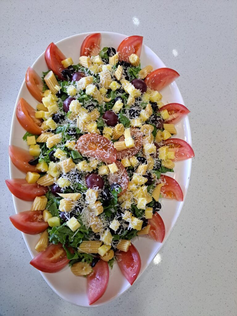 Platter of salad with tomatoes, corn, olives, greens and grated cheese prepared at the villa